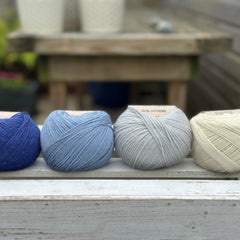 Four balls of wool in royal blue, medium denim blue, silvery grey, and cream. 