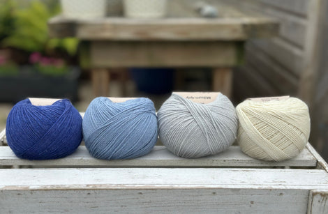 Four balls of wool in royal blue, medium denim blue, silvery grey, and cream. 