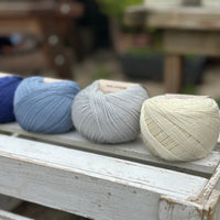 Four balls of wool in royal blue, medium denim blue, silvery grey, and cream. 