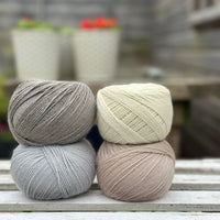 Four balls of wool in medium grey, cream, silvery grey, and oatmeal beige. 