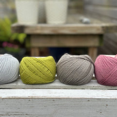 Four balls of wool in silvery grey, rich earthy lime green, medium grey, and medium soft pink. 