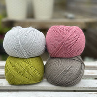 Four balls of wool in silvery grey, rich earthy lime green, medium grey, and medium soft pink. 