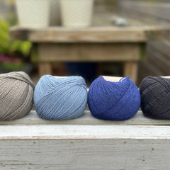 Four balls of wool in mid-grey, medium denim blue, royal blue, and dark grey. 