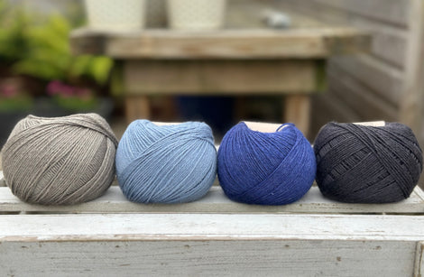 Four balls of wool in mid-grey, medium denim blue, royal blue, and dark grey. 