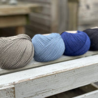 Four balls of wool in mid-grey, medium denim blue, royal blue, and dark grey. 