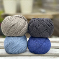 Four balls of wool in mid-grey, medium denim blue, royal blue, and dark grey. 