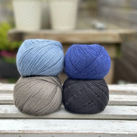 Four balls of wool in mid-grey, medium denim blue, royal blue, and dark grey. 