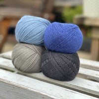 Four balls of wool in mid-grey, medium denim blue, royal blue, and dark grey. 