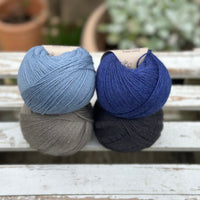 Four balls of wool in mid-grey, medium denim blue, royal blue, and dark grey. 