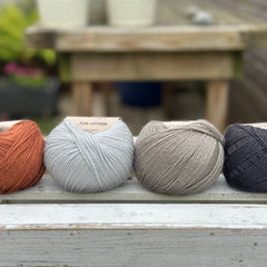 Four balls of wool in rust, silvery grey, medium grey, and dark grey. 