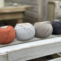 Four balls of wool in rust, silvery grey, medium grey, and dark grey. 