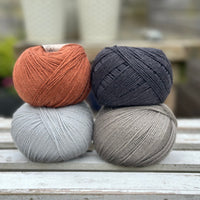 Four balls of wool in rust, silvery grey, medium grey, and dark grey. 