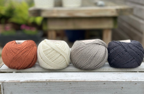 Four balls of wool in rust, cream, mid grey and dark grey.