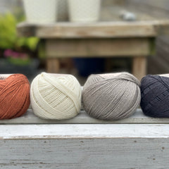 Four balls of wool in rust, cream, mid grey and dark grey.