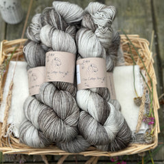 Five skeins of hand dyed yarn which are a variegated mix of shades of grey, from cream to charcoal.