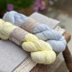 two different skeins of hand dyed yarn: one is very light yellow and one is light blue. 