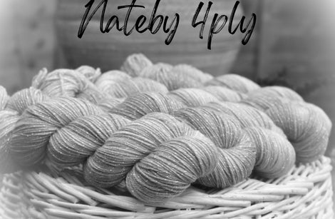 A black and white image of four skeins of yarn resting on a wicker basket. The yarn appears lightly variegated and has a thread of silver sparkle running throughout it. Nateby 4ply is written across the top of the image in black text