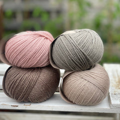 Four balls of yarn in two piles of two balls. On the left there is a pink ball and a brown ball. On the right there is a grey balls and a beige ball