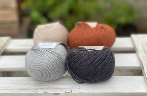 Four balls of yarn in two rows of two balls. On the left there is a beige ball and a pale blue ball. On the right there is a reddish brown ball and a dark grey ball