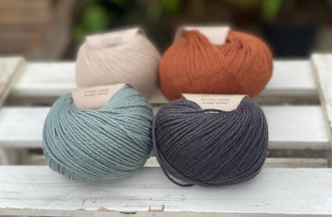 Four balls of yarn in two rows of two balls. On the left there is a beige ball and a blue-green ball. On the right there is a reddish brown ball and a dark grey ball