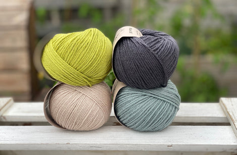 Four balls of yarn in two rows of two. There is a green ball, a dark grey ball, a beige ball and a blue-green ball.