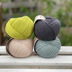 Four balls of yarn in two rows of two. There is a green ball, a dark grey ball, a beige ball and a blue-green ball.