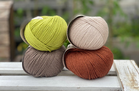 Four balls of yarn in two rows of two. There is a beige ball, a brown ball, a reddish-brown ball and a green ball.