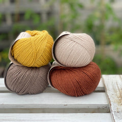 Four balls of yarn in two rows of two. There is a beige ball, a brown ball, a reddish-brown ball and a yellow ball.