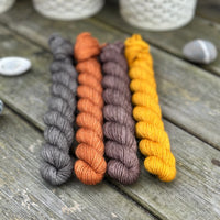 Four mini skeins. From left to right - a dark grey skein, a reddish brown skein, a brown skein and a deep yellow skein