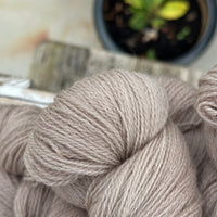 Close up image of the texture of a skein of light brown laceweight yarn