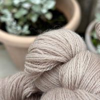 Close up image of the texture of a skein of light brown laceweight yarn