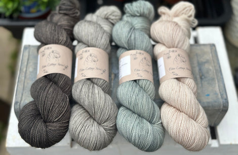 Four skeins of yarn. From left to right: a dark grey skein, a grey skein, a blue-grey skein and a beige skein