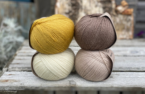 Four balls of yarn. Colours are natural cream, beige, yellow and brown