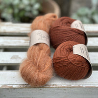 A skein of fluffy reddish-brown yarn with two balls of reddish-brown yarn