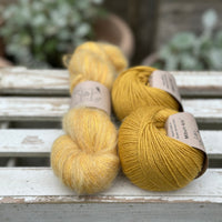 A skein of fluffy yellow yarn with two balls of yellow yarn