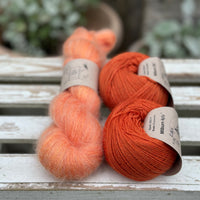 A skein of fluffy orange yarn with two balls of orange yarn