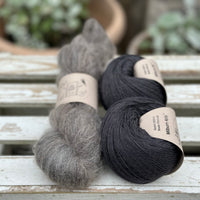 A skein of fluffy dark grey yarn wth two balls of black yarn