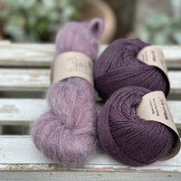 A skein of fluffy purple yarn with two balls of dark purple yarn