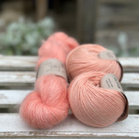 A skein of fluffy pink yarn with two balls of peachy orange yarn