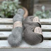 A skein of fluffy grey yarn with two balls of grey yarn