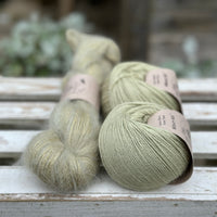 A skein of fluffy green yarn alongside two balls of pale green yarn