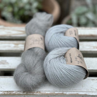 A skein of fluffy grey yarn alongside 2 balls of pale blue yarn 