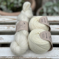 A skein of natural cream coloured yarn alongside two balls of natural cream coloured yarn