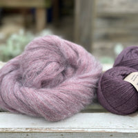 A swirl of fluffy purple yarn with two balls of dark purple yarn