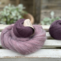 A swirl of fluffy purple yarn with two balls of dark purple yarn