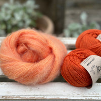 A swirl of fluffy orange yarn with two balls of orange yarn