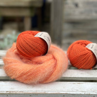 A swirl of fluffy orange yarn with two balls of orange yarn