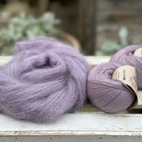 A swirl of fluffy purple yarn with two balls of purple yarn