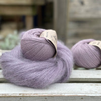 A swirl of fluffy purple yarn with two balls of purple yarn