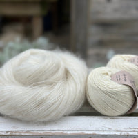 A swirl of natural cream coloured yarn alongside two balls of natural cream coloured yarn